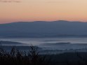 Blick aus dem Göttinger Wald über eine teilweise vom Morgennebel verhüllte Landschaft Richtung Harz mit dem Brocken (höchste Erhebung im Bild)