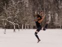 Junge Frau in Sportkleidung springt in einer verschneiten Landschaft in die Luft.