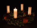 Adventskranz mit weißen Kerzen, von denen eine zum 1. Advent brennt.