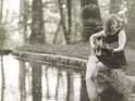Eine Frau spielt an einem Teich auf einer Gitarre und hat ihre Fe dabei im Wasser.