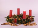 Eine Kerze brennt zum 1. Advent auf einem Adventskranz mit Orangenscheiben und Zimtstangen vor weißem Hintergrund.