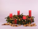 Vier Kerzen brennen zum 4. Advent auf einem Adventskranz mit Orangenscheiben und Zimtstangen vor weiem Hintergrund.