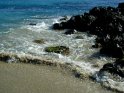 Wellen treffen neben schwarzem, vulkanischen Gestein auf den Strand